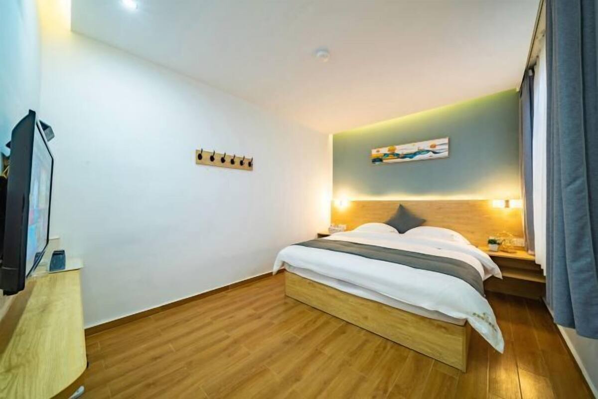A bedroom with a wooden bed, a bedside table, a wall-mounted TV, and a painting.