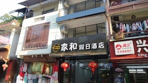A hotel with a sign in Chinese characters, a balcony with plants, and a storefront with clothing items visible through the window. - Yangshuo West Street Jiahe Holiday Hotel (Longtoushan Wharf Branch) (Yangshuo)