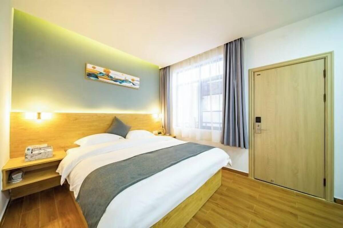 A hotel room with a bed, bedside table, nightstand, and a painting on the wall.