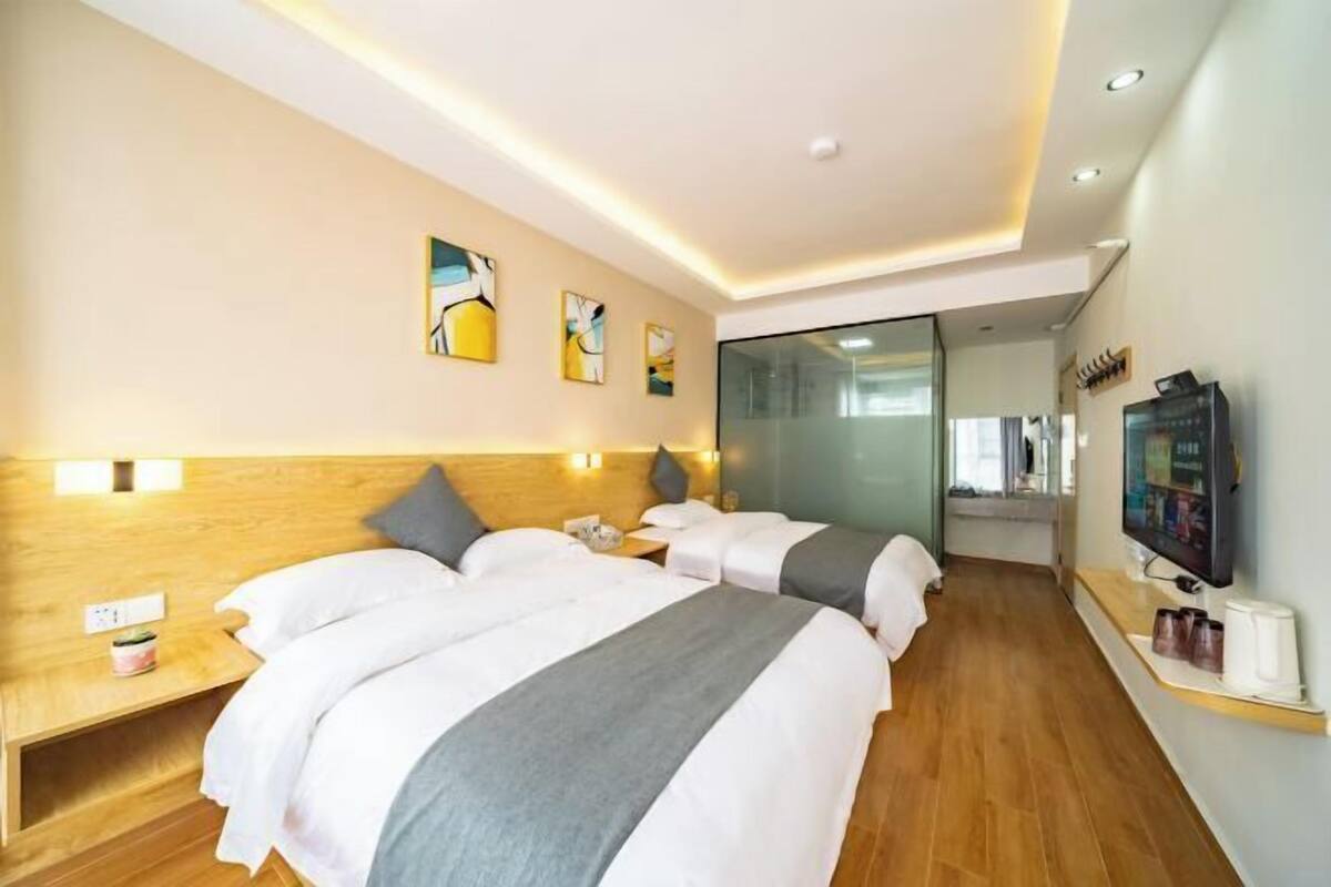 A hotel room with two beds, wooden headboards, a flat-screen TV, and artwork on the walls.