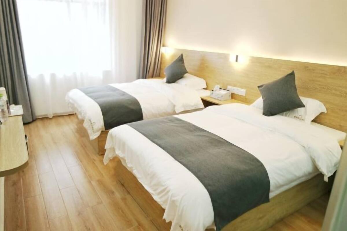 A hotel room with two beds, wooden flooring, and a nightstand with a phone and tissues.