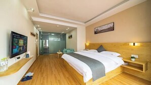 A hotel room with a wooden floor, a bed with white bedding, a TV on the wall, and a small table with a plant. - Yangshuo West Street Jiahe Holiday Hotel (Longtoushan Wharf Branch) (Yangshuo)
