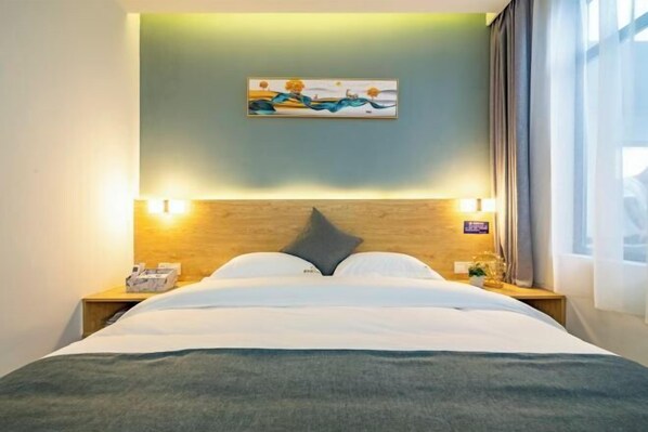 A hotel room with a bed, a painting on the wall, and a nightstand with a lamp.