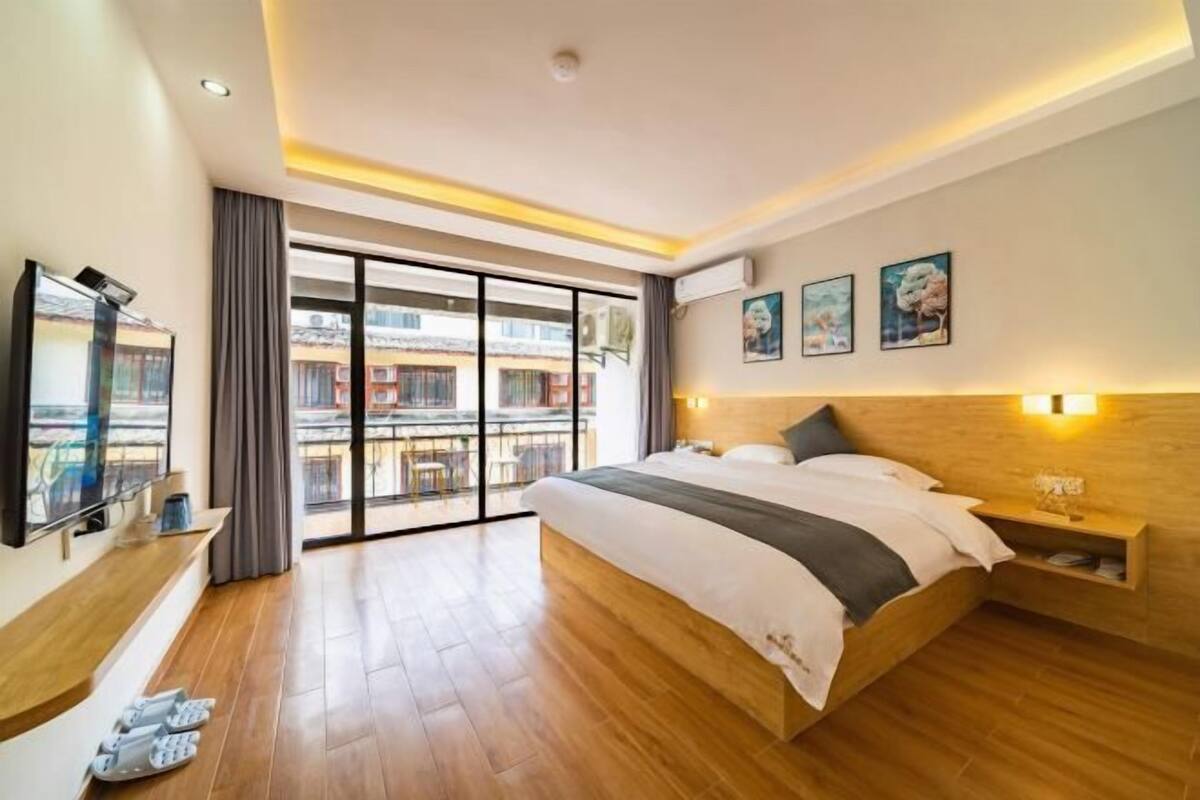 A modern hotel room with a large bed, a TV, a balcony with a view, and artwork on the wall.
