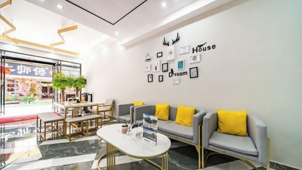 A hotel lobby with a check-in desk, a sofa with yellow cushions, a coffee table, and a wall decorated with framed pictures and the words "House" and "Dream". - Yangshuo West Street Jiahe Holiday Hotel (Longtoushan Wharf Branch) (Yangshuo)