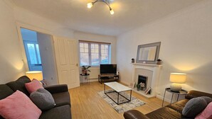 A living room with two sofas, a coffee table, a TV, a fireplace, and a door leading to another room. - Sigerson House Long Stay Discounts Free Parking (Swindon)