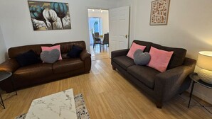 A living room with two sofas, a coffee table, and a rug. There is a painting on the wall and a door leading to another room. - Sigerson House Long Stay Discounts Free Parking (Swindon)