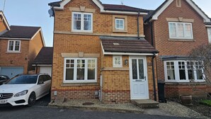A two-story house with a garage, a white car parked in front, and a small garden area. - Sigerson House Long Stay Discounts Free Parking (Swindon)