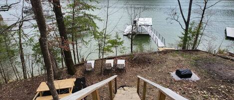 A wooden deck leading to a dock over water, surrounded by trees and a picnic table.