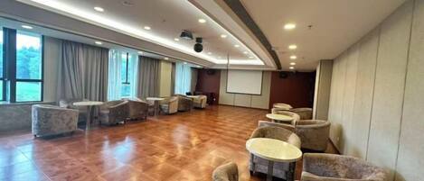 A spacious room with a long table and chairs, a projector screen, and a large window.