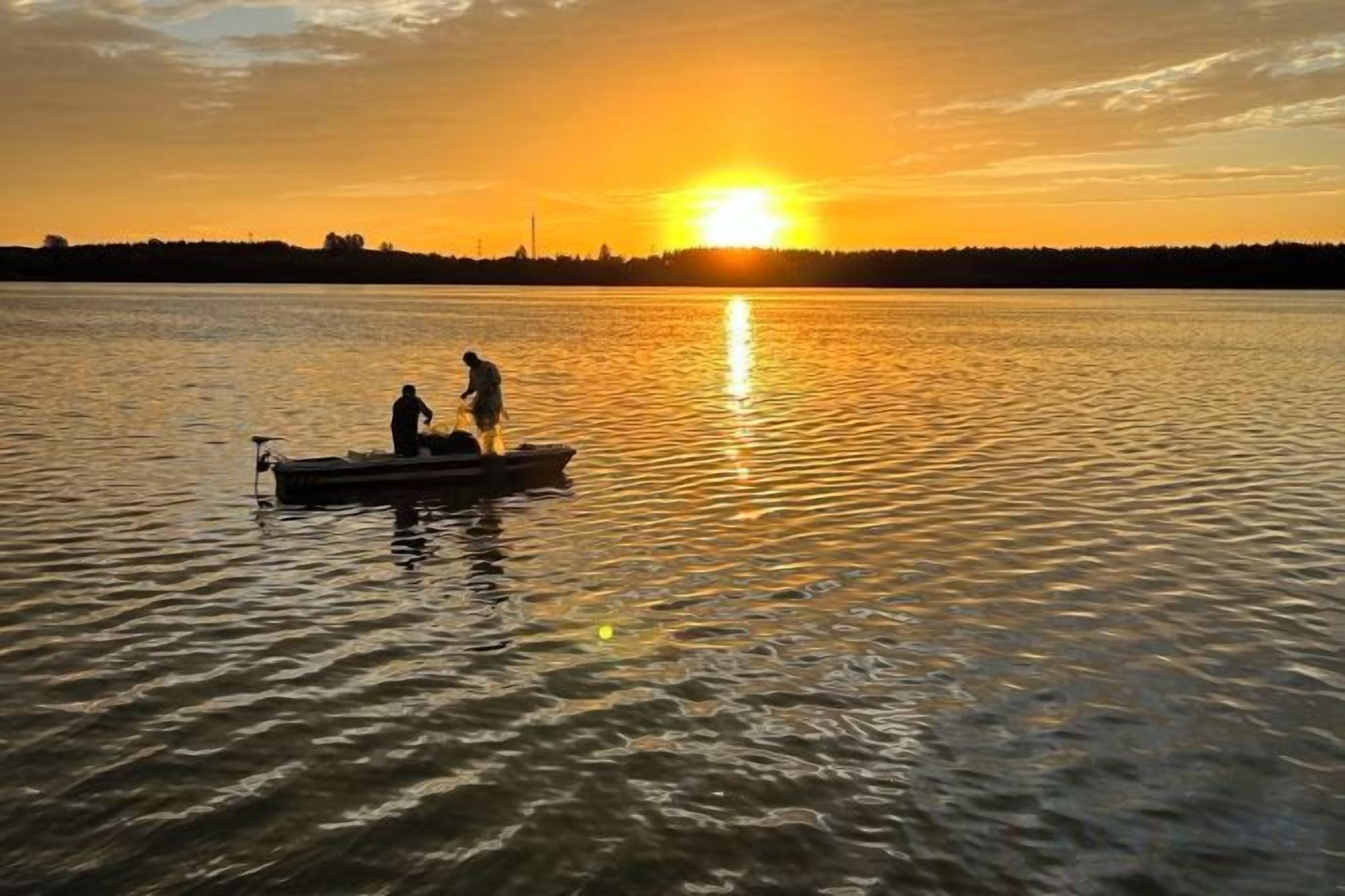 Ein Boot auf ruhigem Wasser bei Sonnenuntergang, mit zwei Personen an Bord.