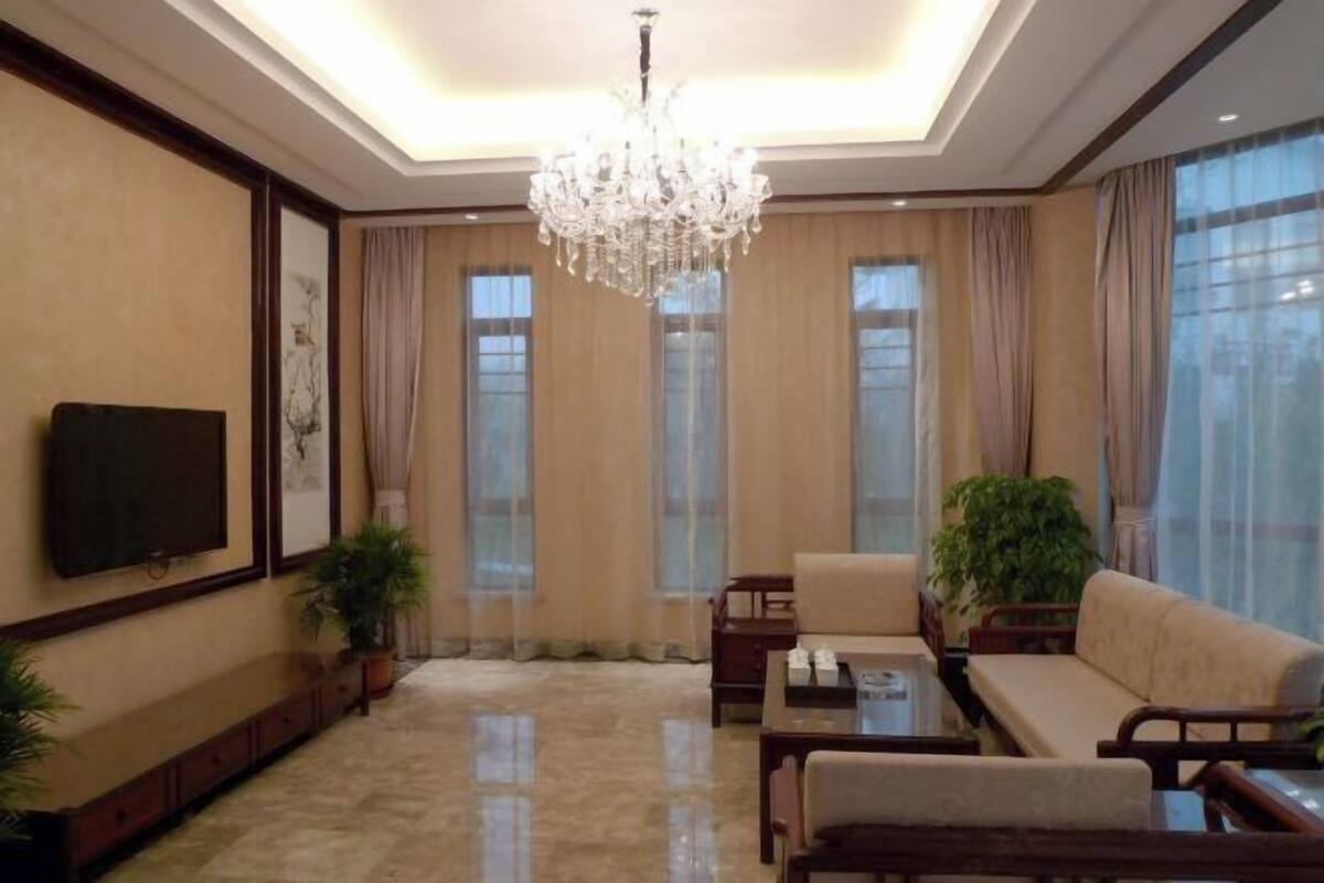 A spacious living room with a chandelier, a sofa, a coffee table, and a television mounted on the wall.