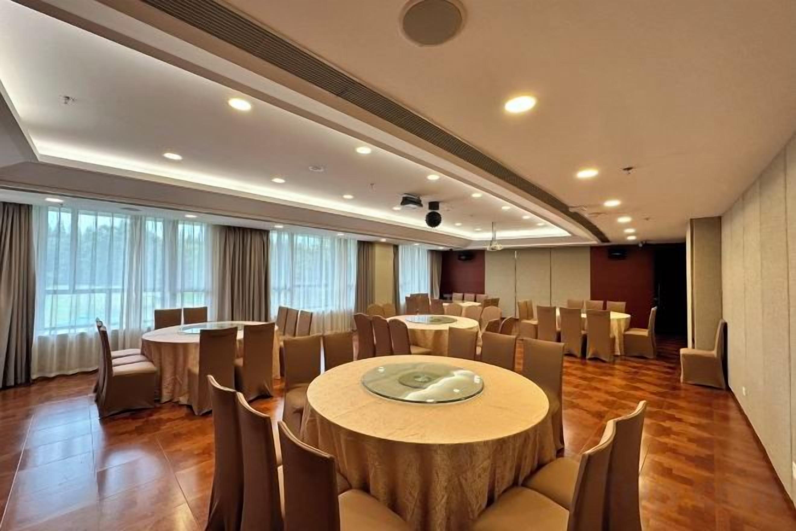 Sala de conferência com mesas redondas, cadeiras e uma tela grande.