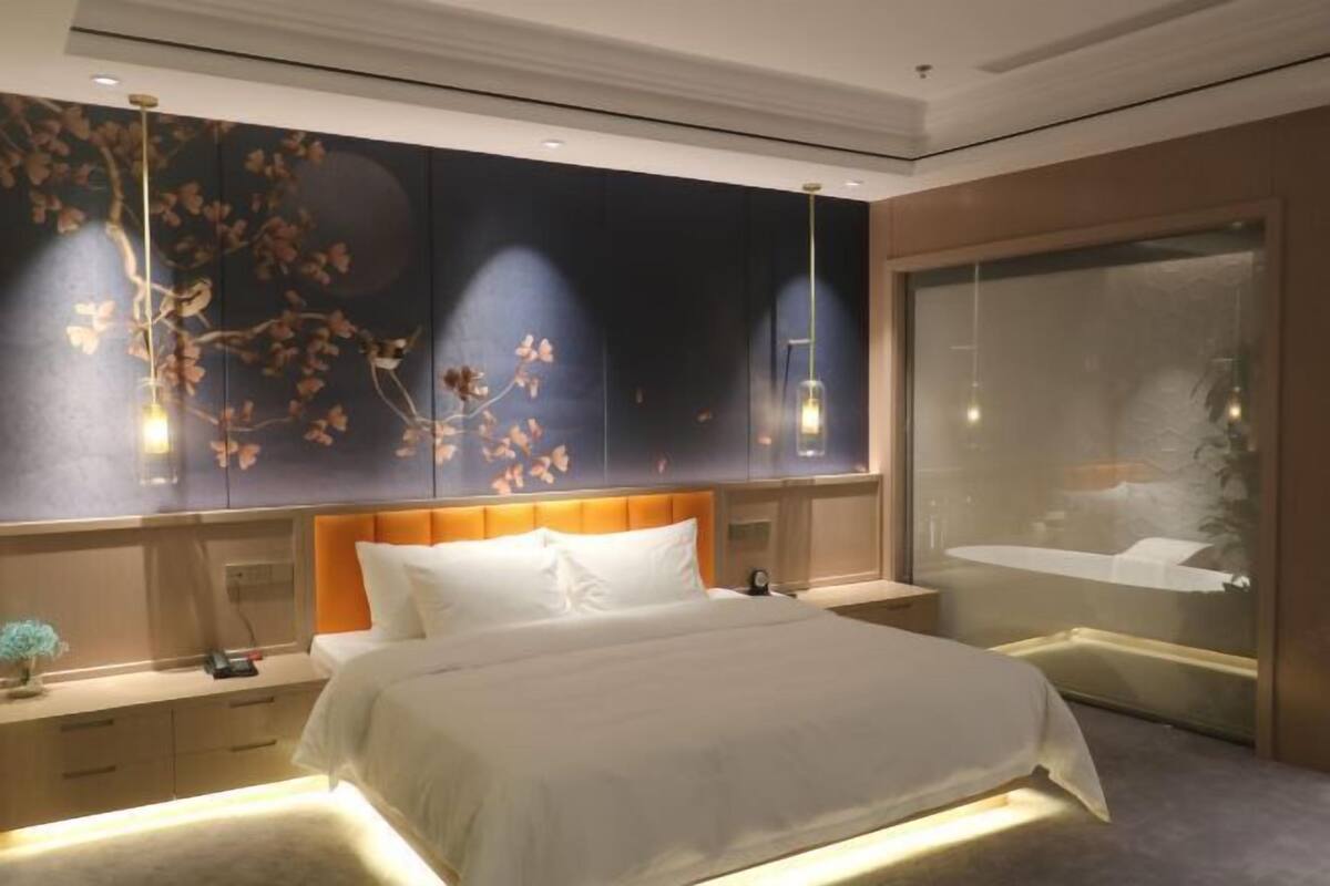 A modern bedroom with a bed, bedside tables, a nightstand, a wall with a floral mural, and a large window with a view.