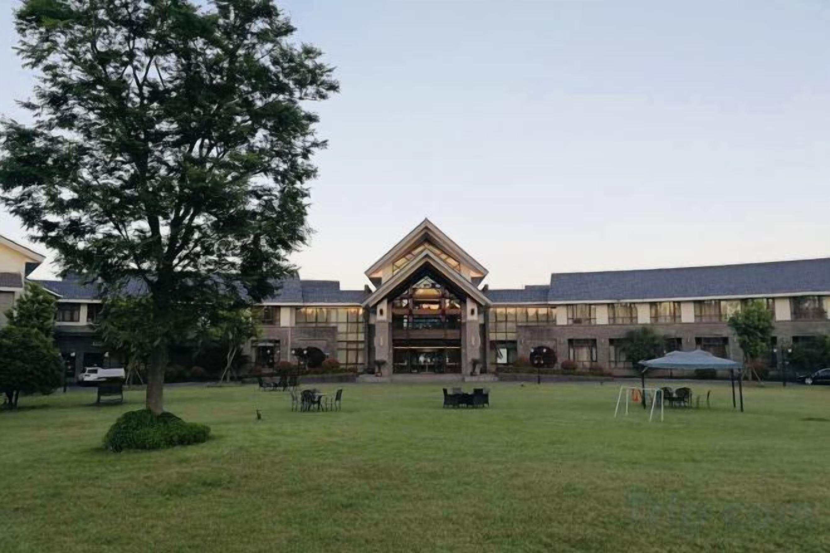 Um edifício com entrada central, rodeado por um gramado e árvores.