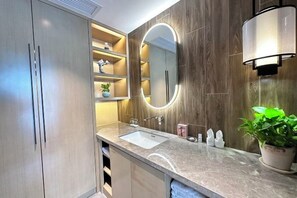 Une salle de bain moderne avec un plan de toilette en marbre, un grand miroir doté d’un éclairage circulaire et des panneaux muraux en bois.