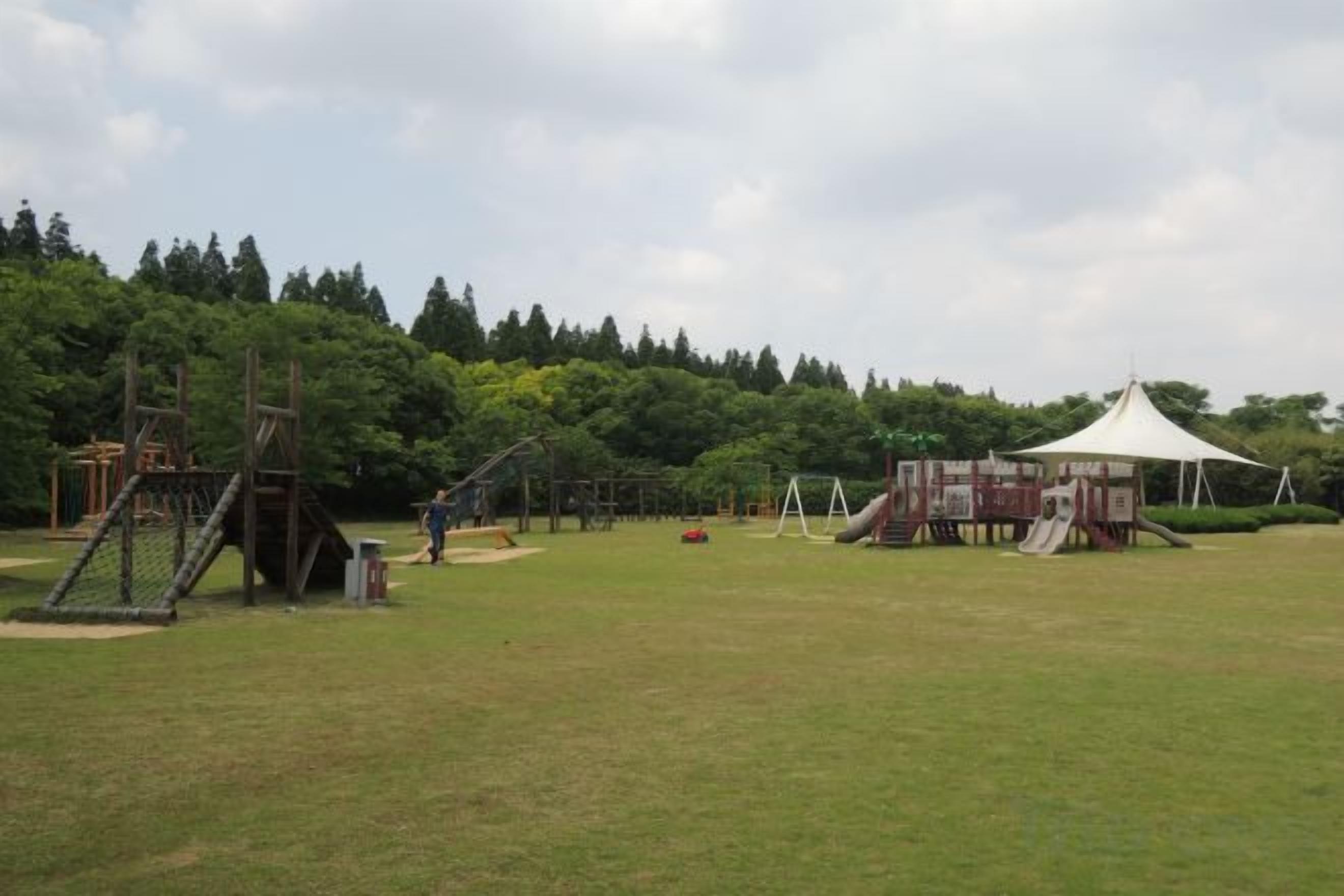 Parque infantil ao ar livre com diversas estruturas de recreação e área de estar coberta.