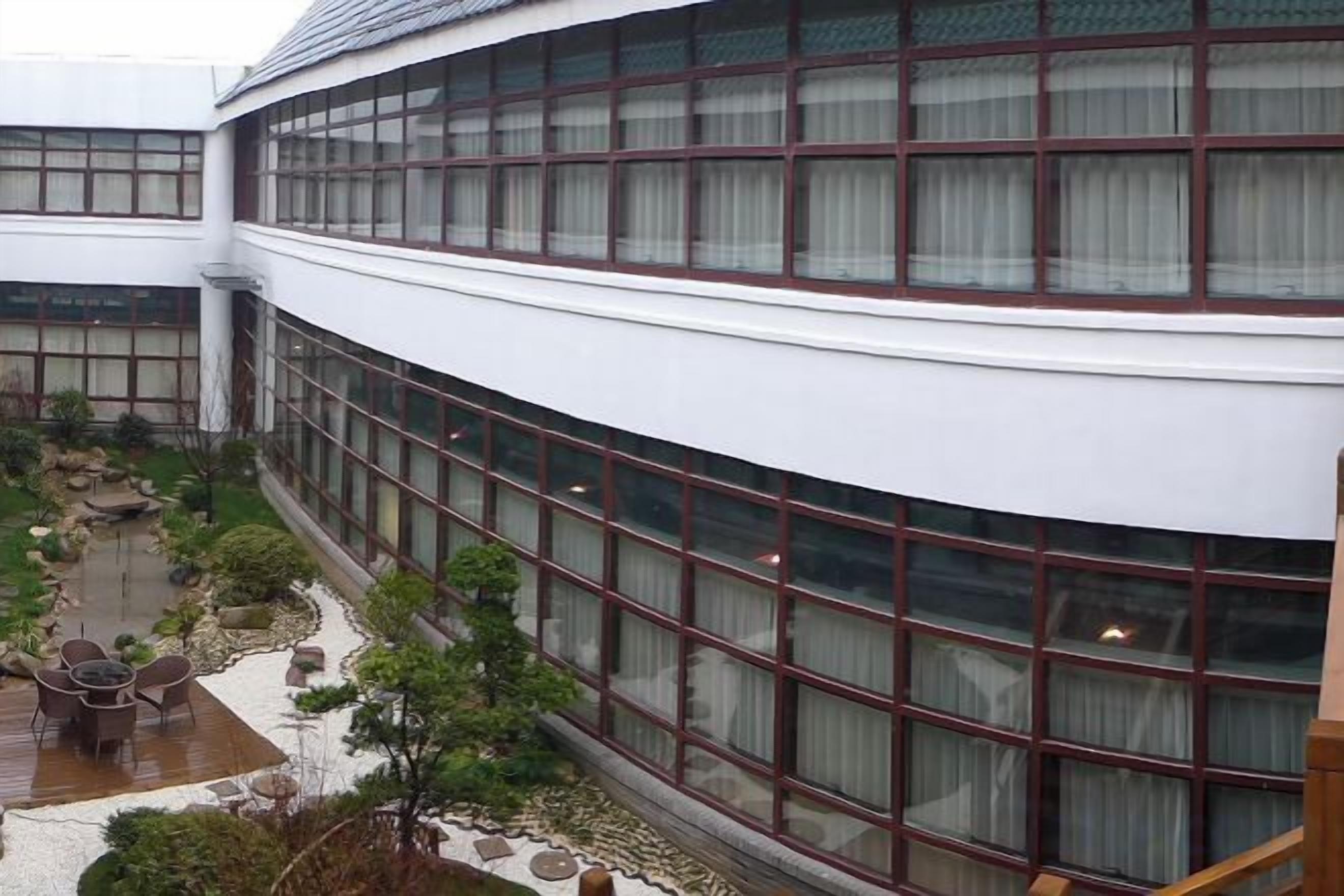 Un edificio de varios pisos con amplios ventanales y un patio con asientos y plantas.