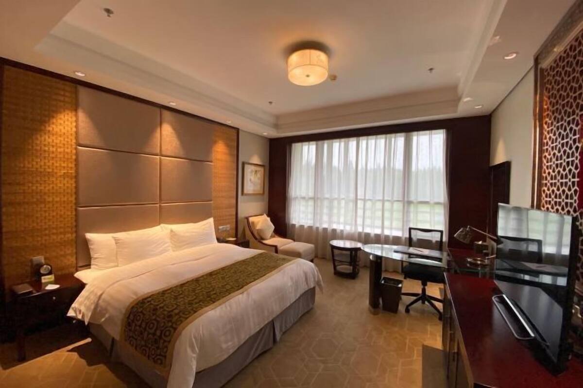 A hotel room with a large bed, a desk, a chair, a TV, and a window with curtains.