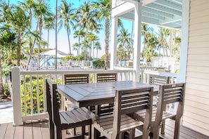 A wooden deck with a table and chairs, surrounded by a white fence, overlooking a pool area with palm trees and lounge chairs. - Duck Key Waterfront Villa w/ 2 Free Kayaks & near 2 Public Marinas (Marathon)