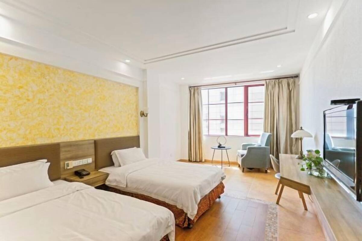Ein Hotelzimmer mit zwei Betten, einem Schreibtisch, einem Stuhl, einem Fernseher und einem Fenster mit Vorhängen.