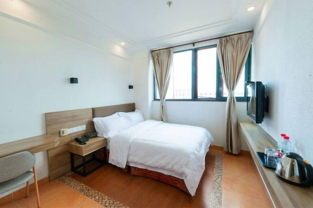 Ein Hotelzimmer mit Bett, Schreibtisch, Stuhl, Fernseher und einem Fenster mit Vorhängen.