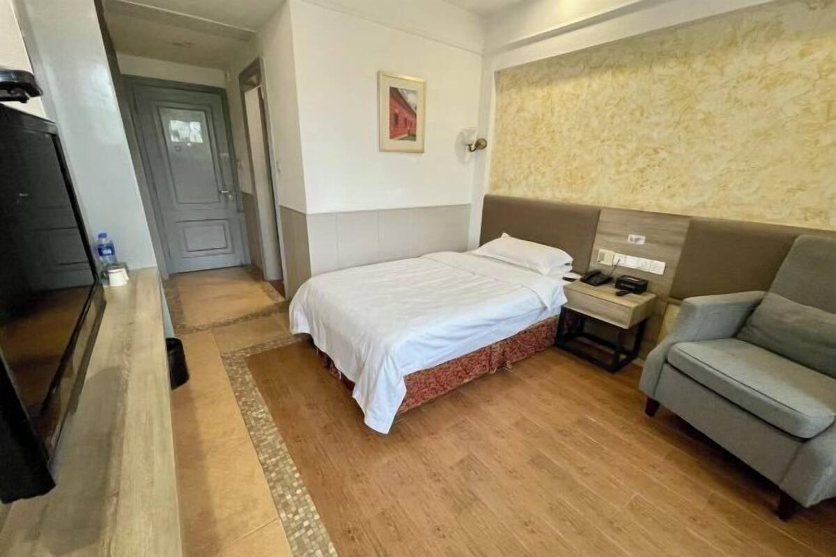 Ein Hotelzimmer mit Bett, Stuhl, Nachttisch, Wandlampe und einer Tür.