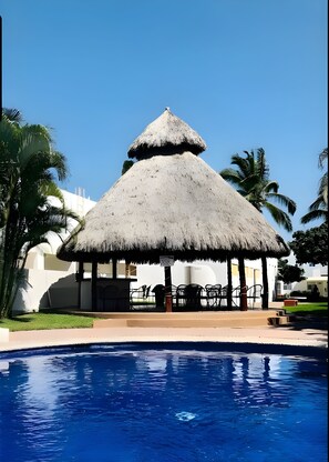 A thatched-roof structure with a pool in the foreground.