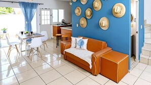 Uma sala de estar moderna com uma parede azul de destaque, um sofá, uma área de jantar com mesa e cadeiras e uma cozinha ao fundo.