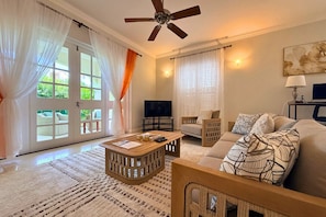 A living room with a ceiling fan, a television, a sofa, a coffee table, and a large window with curtains.