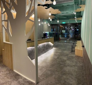 A modern interior with a reception desk, seating area, and a tree-like decorative partition. - New City Hotel (Taipei)