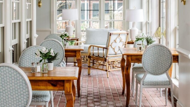 A dining area with brick flooring, white chairs, a wooden table, and a chandelier.