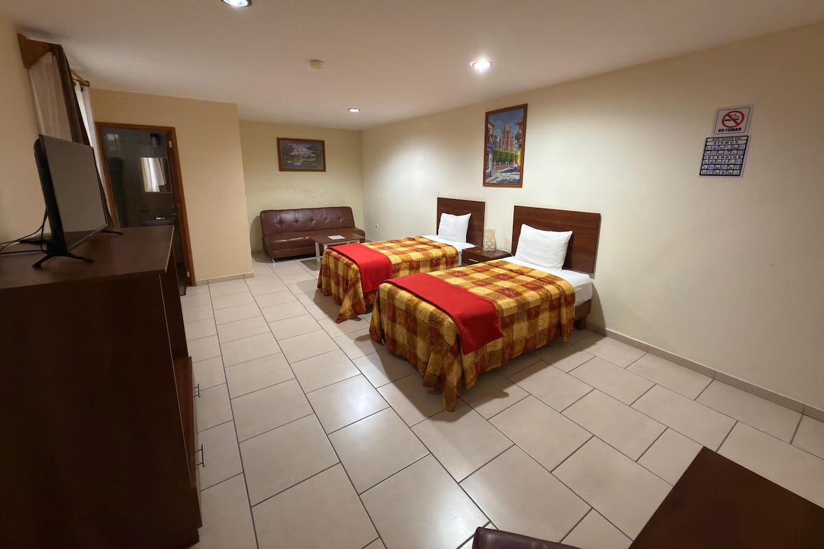 A hotel room with two beds, a desk, a couch, and a TV.