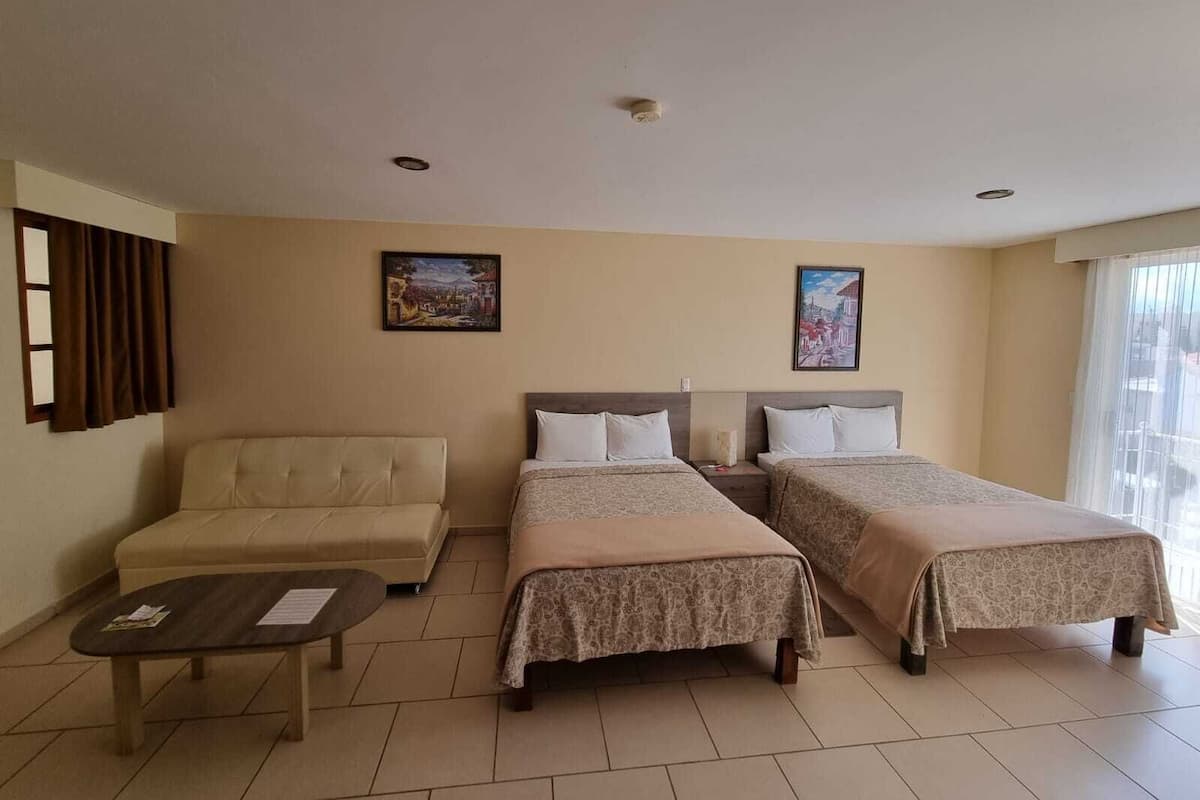 A hotel room with two single beds, a sofa, a small table, and two paintings on the walls.