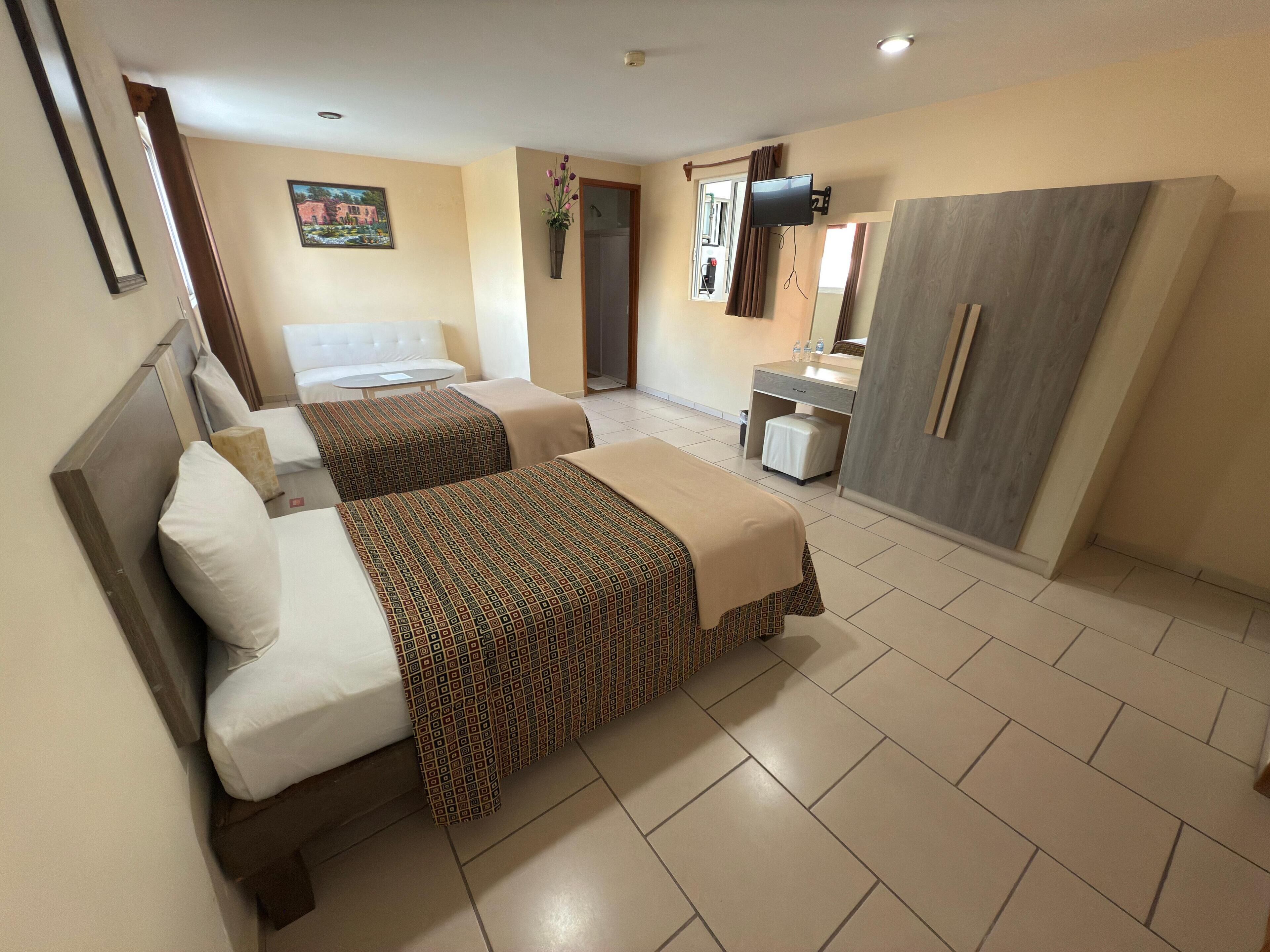 A hotel room with two beds, a desk, a chair, a TV, and a wardrobe.