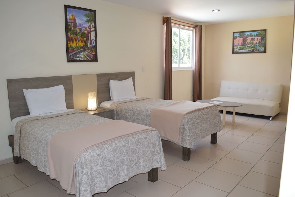 A hotel room with two beds, a sofa, a small table, and two paintings on the walls.