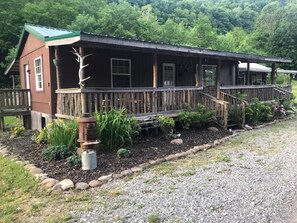 A rustic cabin with a porch, a staircase, and a garden area with plants and rocks.