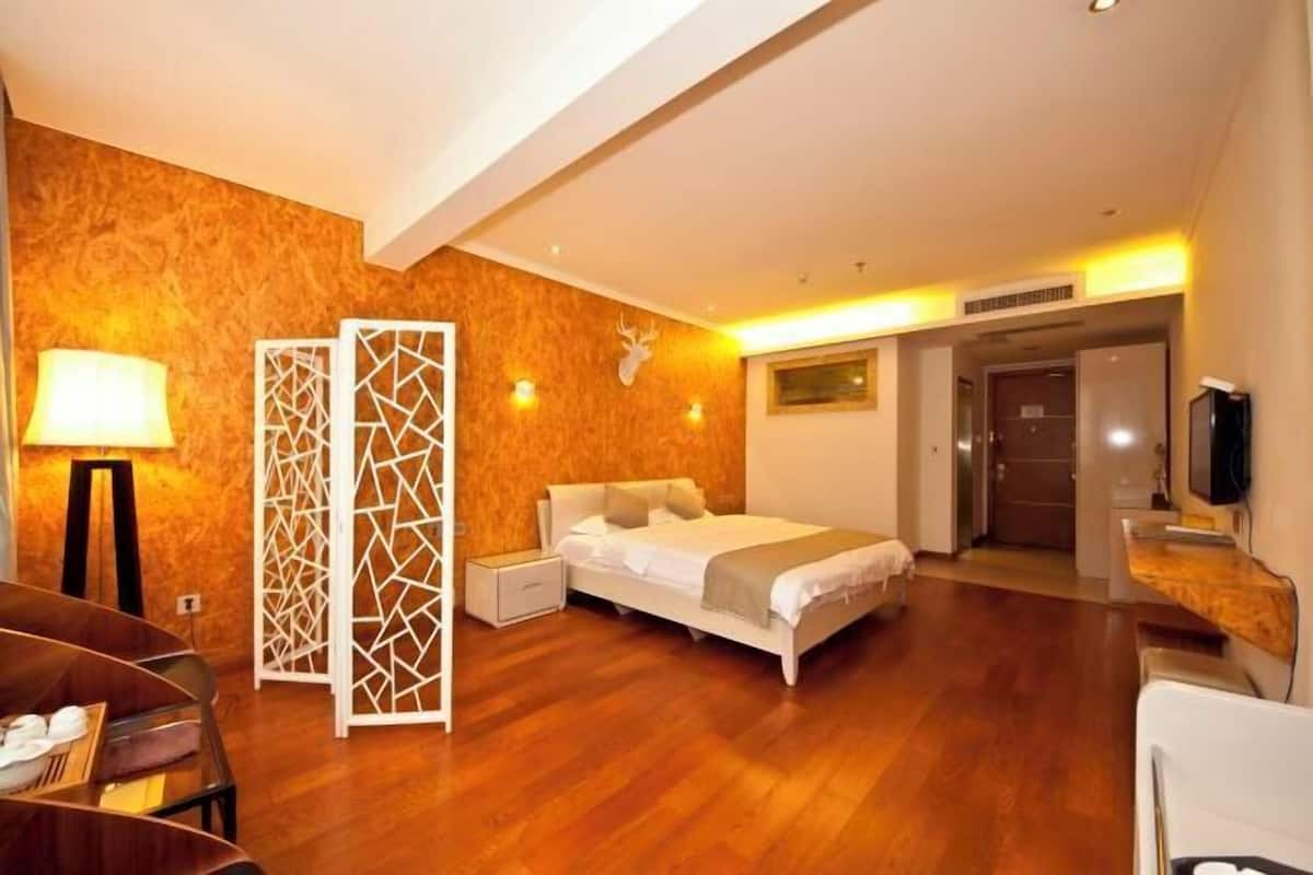 A hotel room with a bed, a desk, a chair, a TV, a lamp, and a decorative wall panel.