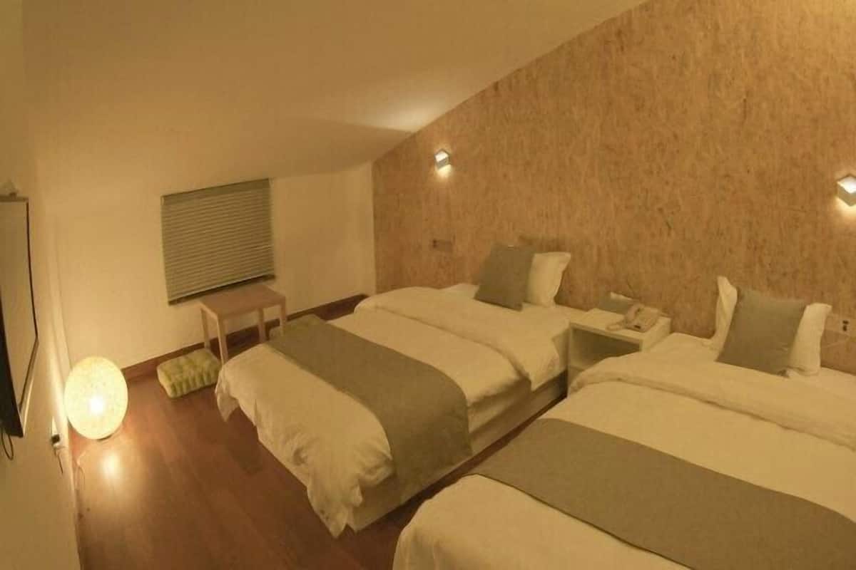 A hotel room with two beds, a bedside table, a lamp, and a window with blinds.