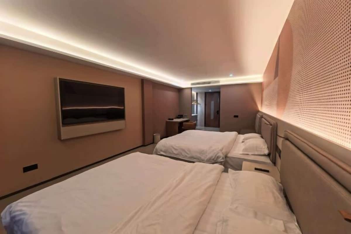 A hotel room with two beds, a flat-screen TV, a window with blinds, and a door leading to another room.
