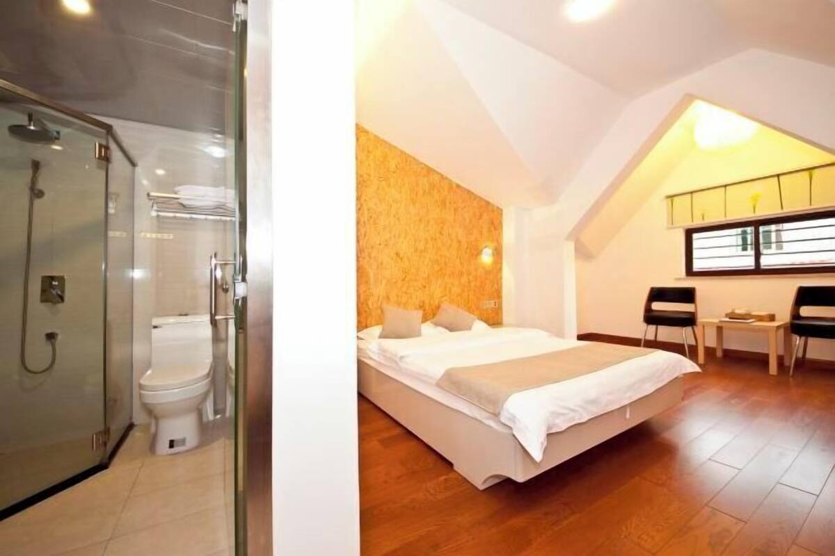 A bedroom with a bed, a shower, a toilet, and a small table with chairs.
