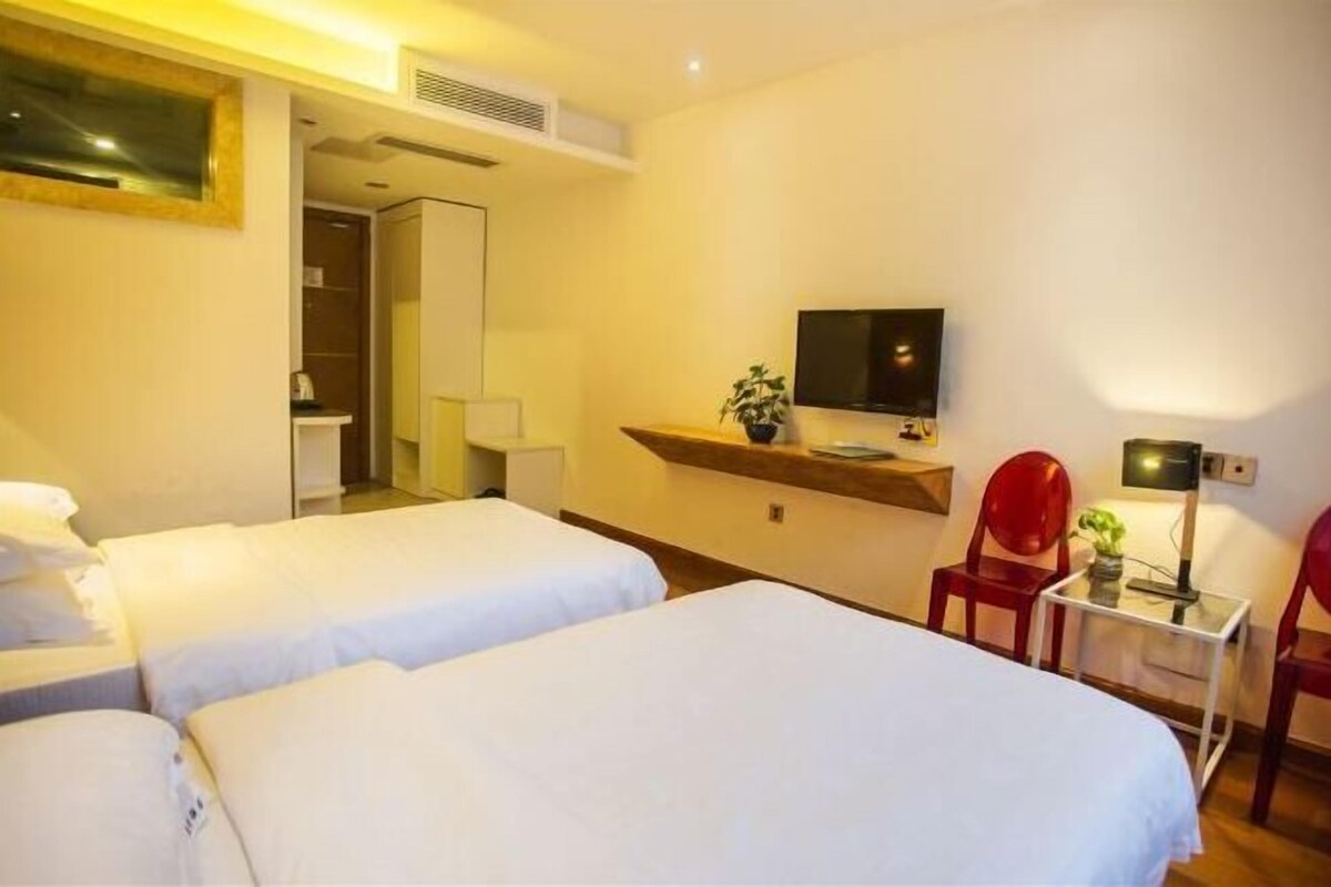 Habitación de hotel con dos camas, un televisor, una mesita con lámpara y una silla roja.