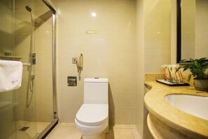 Un baño pequeño con ducha compartimentada por vidrio, inodoro blanco y lavamanos color crema con espejo.