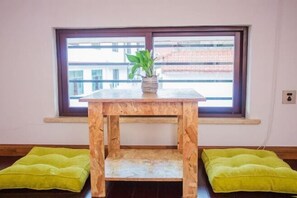 A small wooden table with a plant on top, positioned in front of a window with a view of buildings. - Yilan Hotel (Wuyishan)