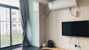 A room with a large window, an air conditioning unit, a mounted television, and a small wooden shelf with a kettle and a cup. - Hengji Hotel (Shanghai Hongkou Football Stadium Dongbaoxing Road Subway Station) (Shanghai)