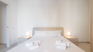 A hotel room with a large bed, two bedside tables with lamps, and neatly folded towels on the bed. - Ada Bright Escape Apartment (Cagliari)