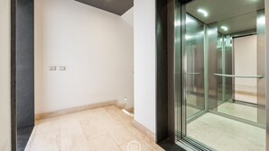 A modern interior with a glass elevator door, a tiled floor, and a plain wall with a light switch. - Ada Bright Escape Apartment (Cagliari)