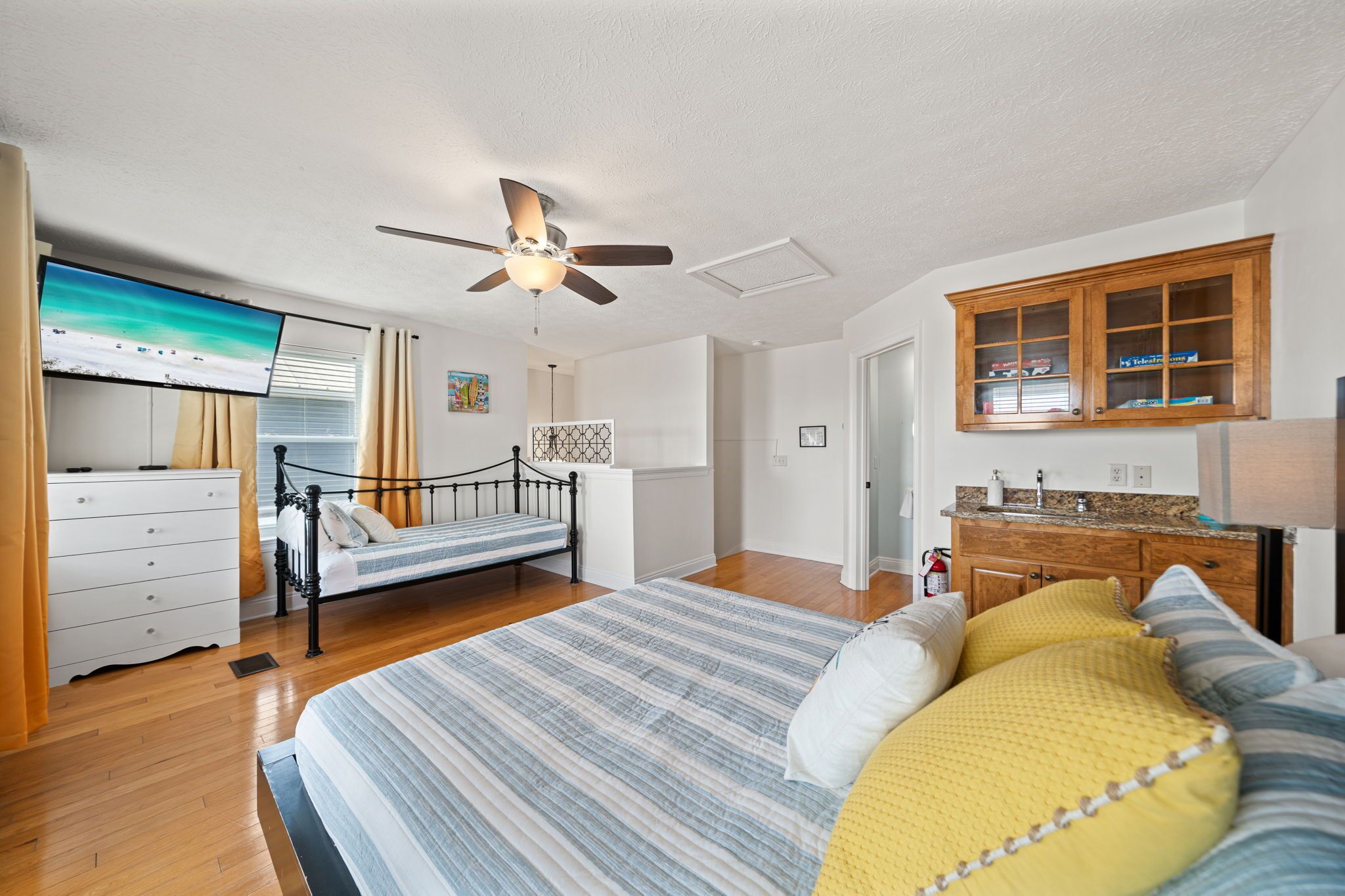A bedroom with a bed, a dresser, a TV, a ceiling fan, and a wooden cabinet.