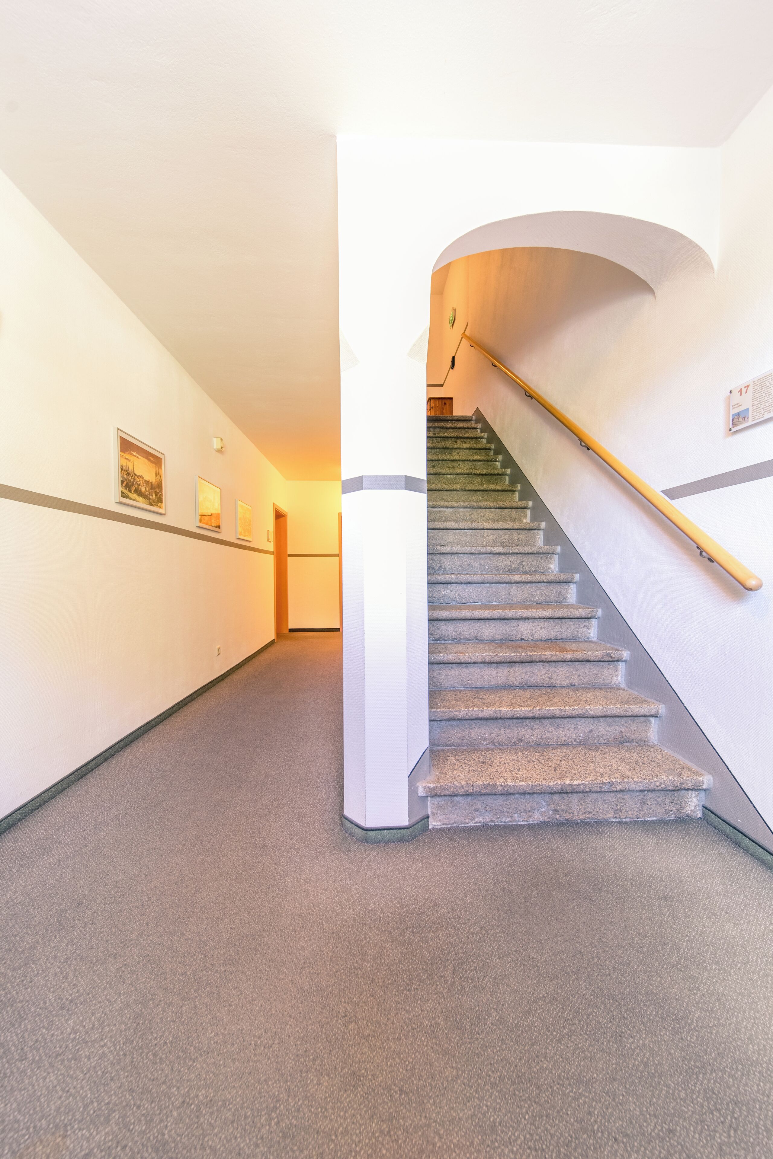 A staircase with a handrail, carpeted floor, and framed pictures on the walls.