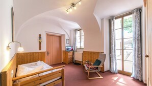 A room with a wooden bed, a wooden chair, a small table, a radiator, a television, and a window with curtains. - Hotel Zum Hothertor (Görlitz)